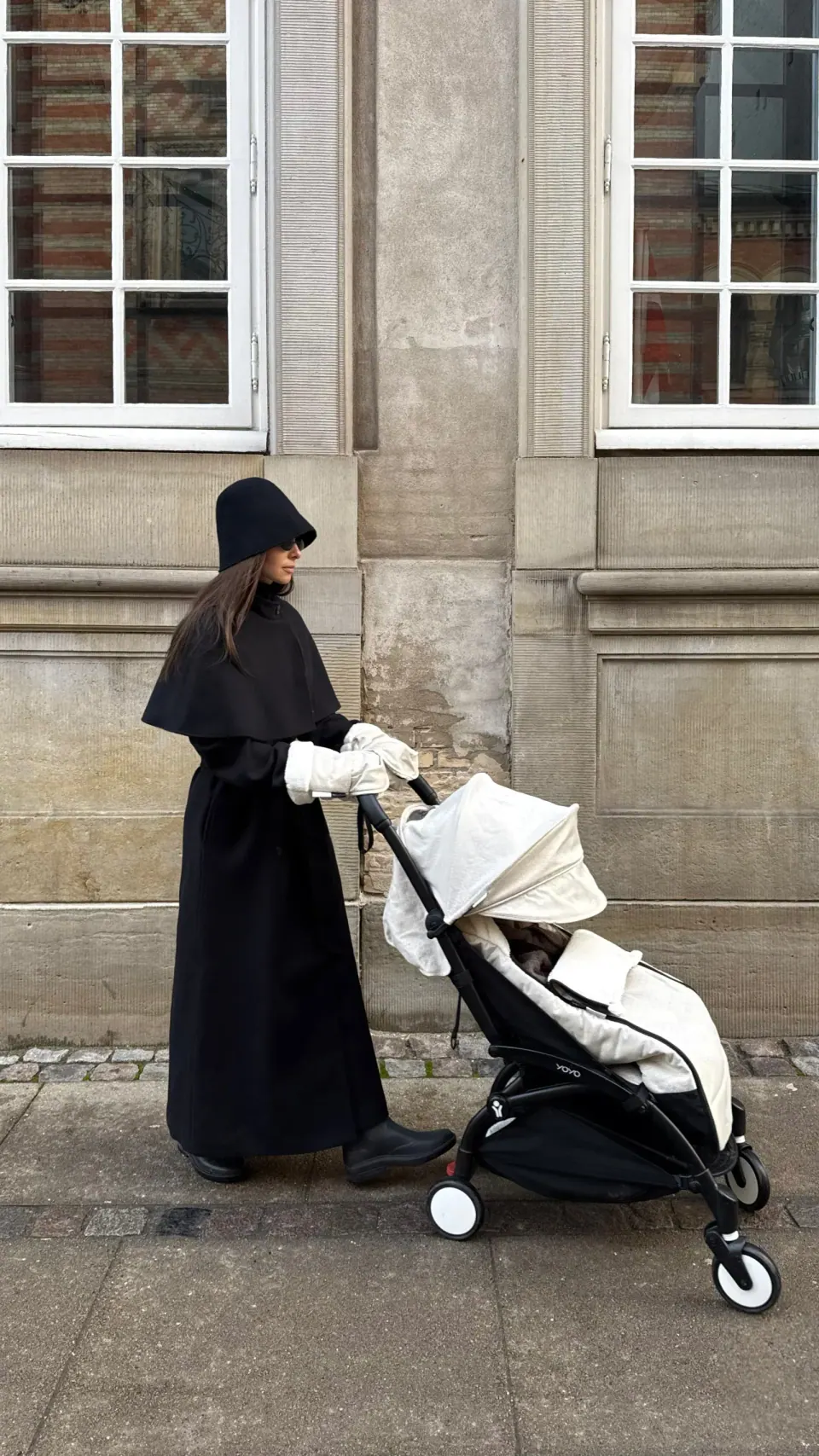 Creator in a black outfit walking with a stroller on a city street