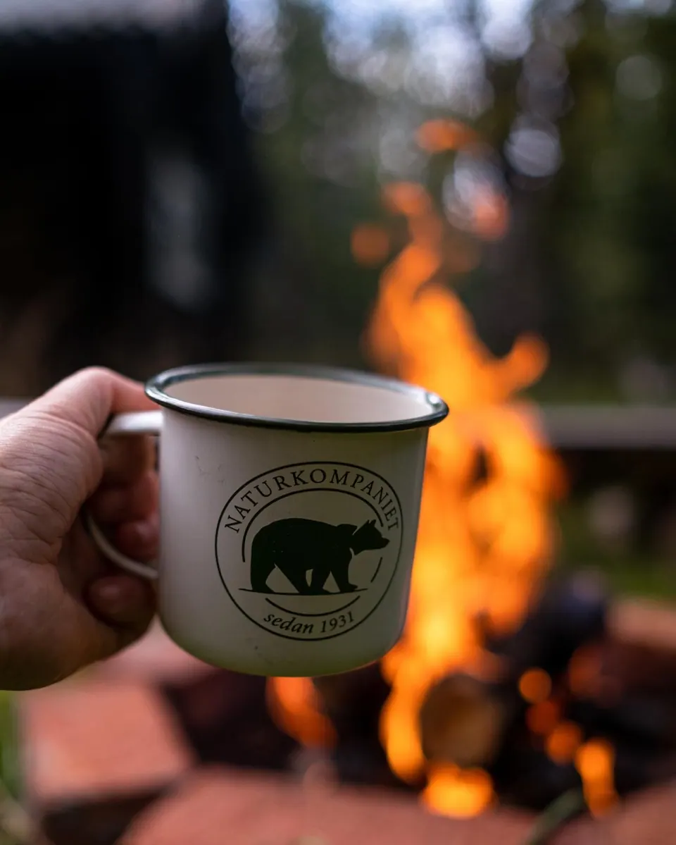 Enamel mug beside a campfire, Naturkompaniet campaign